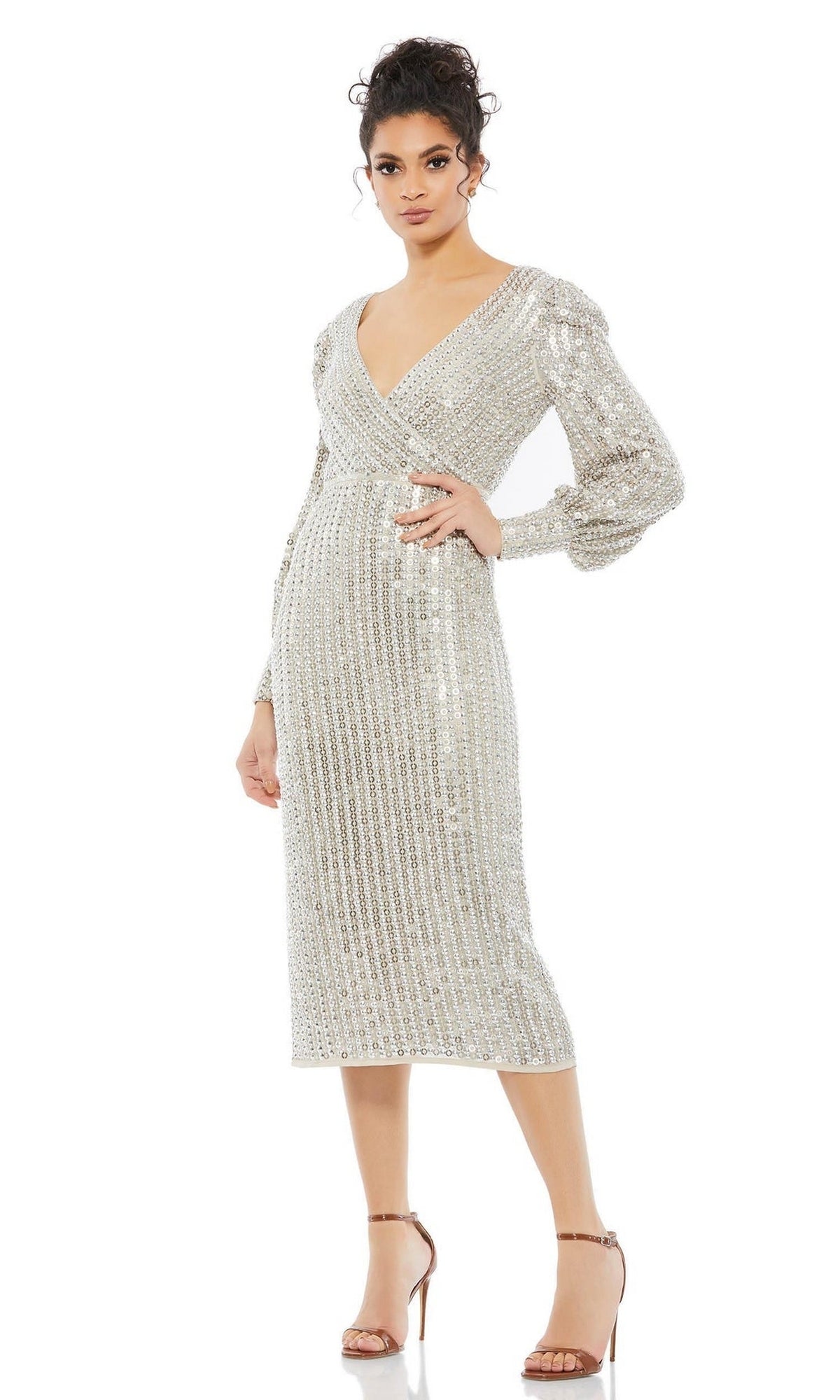 A woman models the Short Wedding Guest Dress 10809 by Mac Duggal—a silver, v-neck, long-sleeve sequin midi fitted dress—paired with strappy high-heeled sandals against a plain white background.